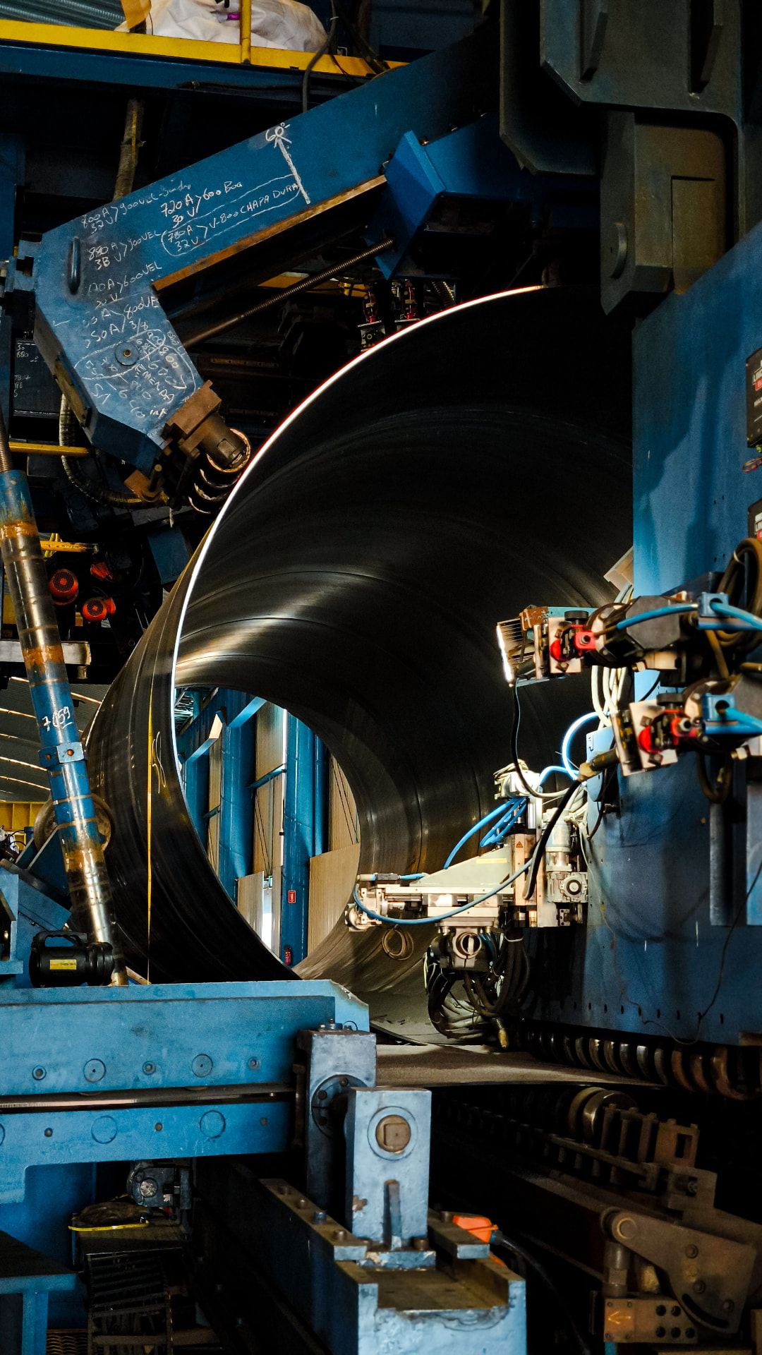 Industrial manufacturing inspection — a large fabricated steel pipe held in a heavy machining station with welding equipment